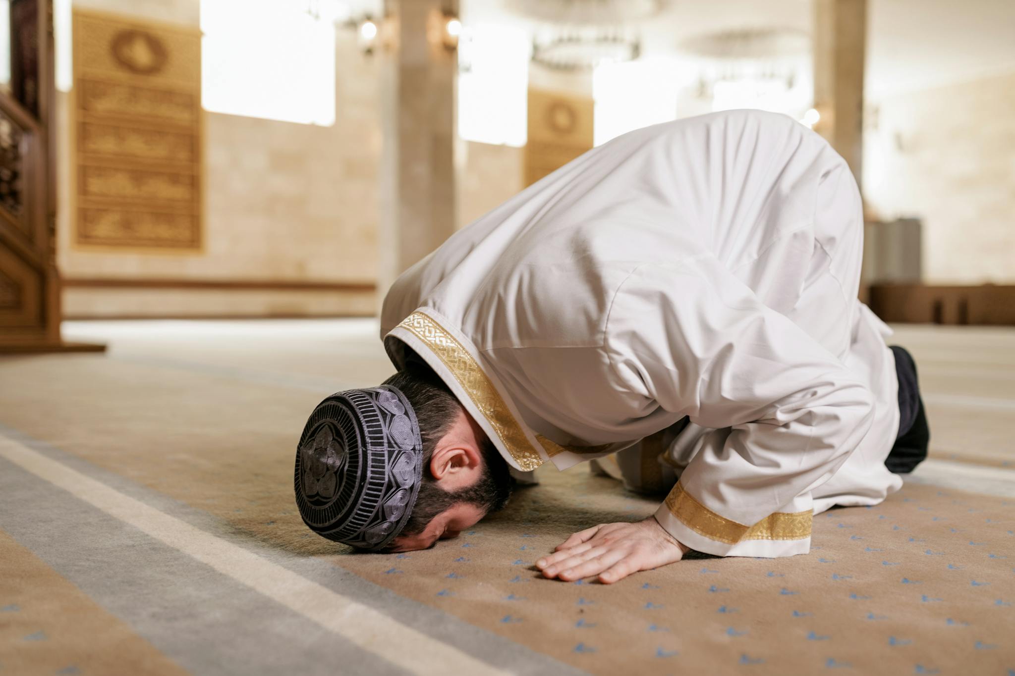 A Muslim man in traditional attire praying inside a mosque, showcasing cultural reverence.