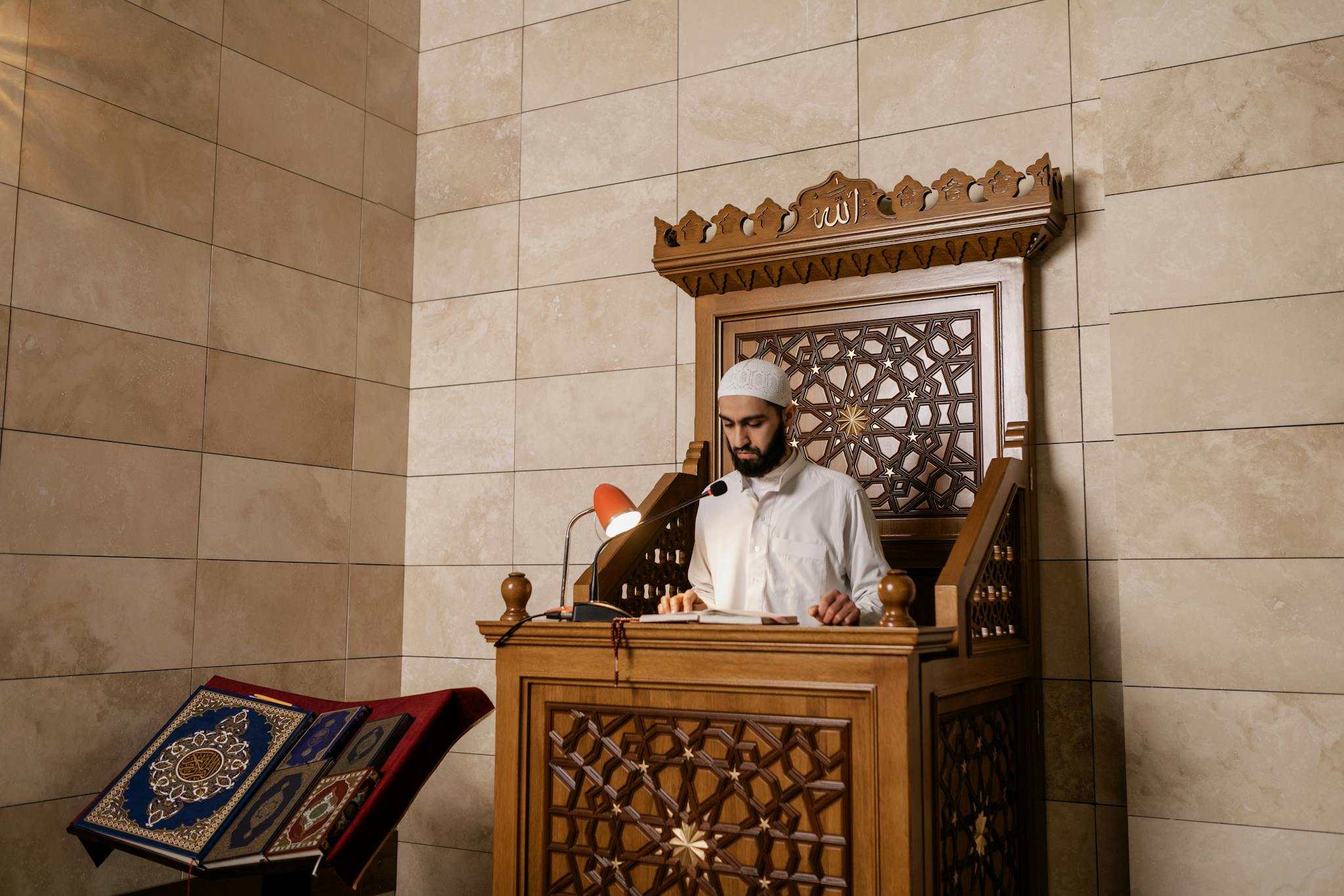 A Muslim man reading the Quran on a decorated mosque pulpit, symbolizing faith and tradition.